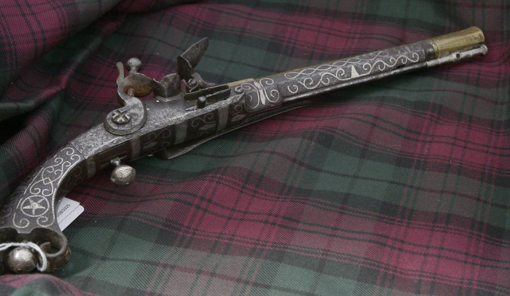 silver flintlock pistol inlayed with engraved scrolling pattern. Sat on a red and green tartan background