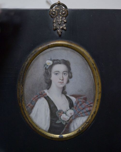 portrait of a young woman with a flower in her hair. A brunette wearing tartan and 18th century costume
